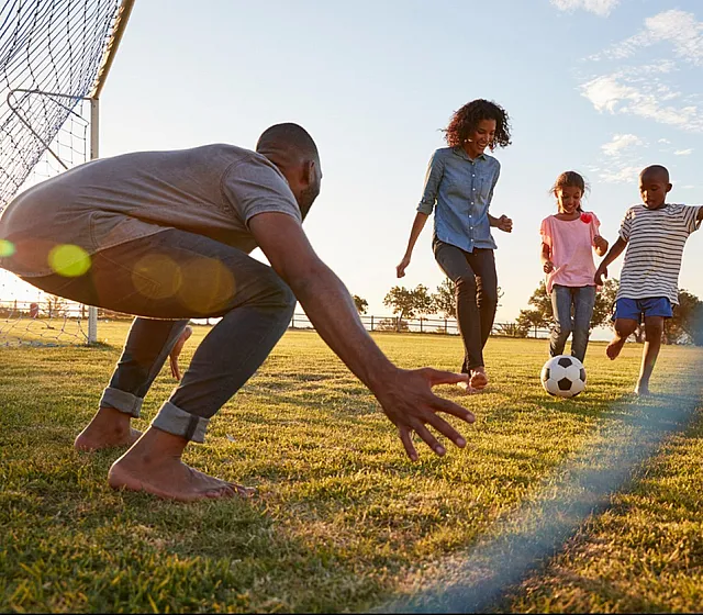 Joyful family playing soccer together on a sunny day, showcasing a vibrant community lifestyle.