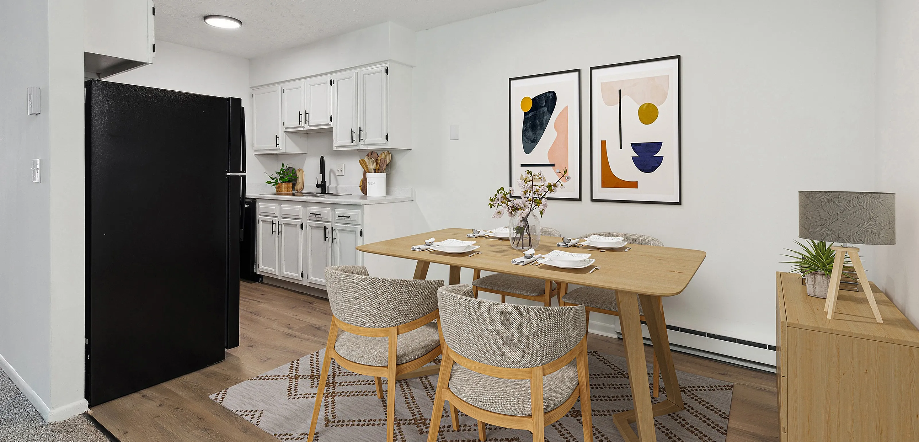 Modern kitchen and dining area featuring sleek black appliances, elegant white cabinetry, and a stylish wooden dining table set under contemporary art.