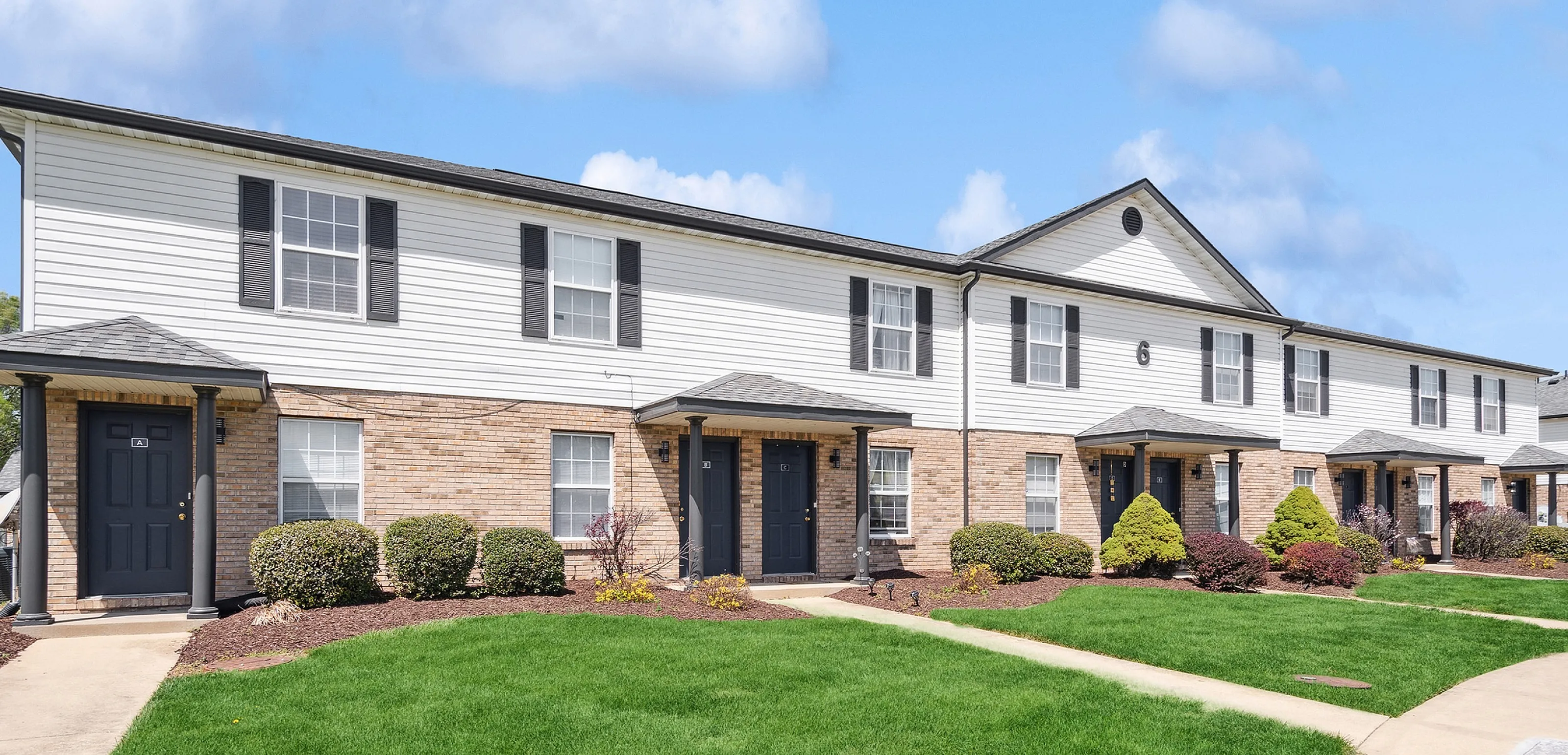 Charming townhouse exterior with well-maintained lawns, picturesque pathways, and inviting entrances under a clear blue sky.
