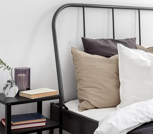 Cozy bedroom corner with elegant pillows, stylish metal bed frame, and a chic bedside table with books and a decorative vase.