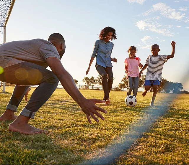 Joyful family playing soccer in a sunny park, showcasing outdoor family fun.