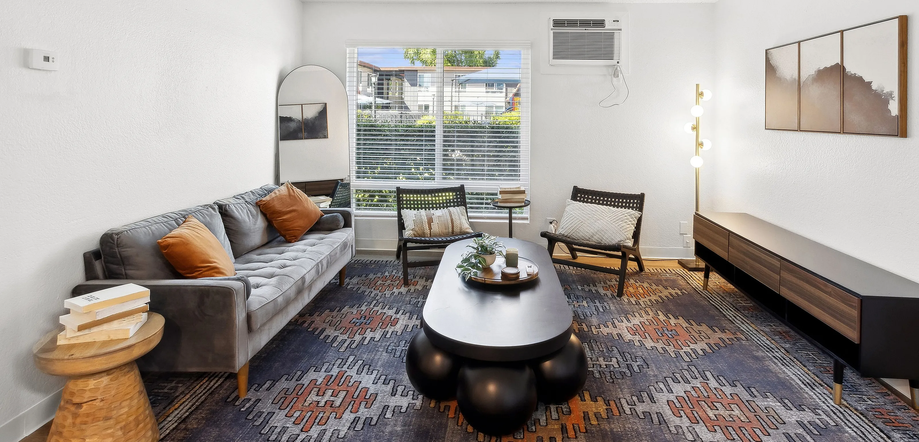 Modern living room with a cozy gray sofa, chic accent chairs, unique coffee table, and a stylish geometric rug, highlighted by natural light.