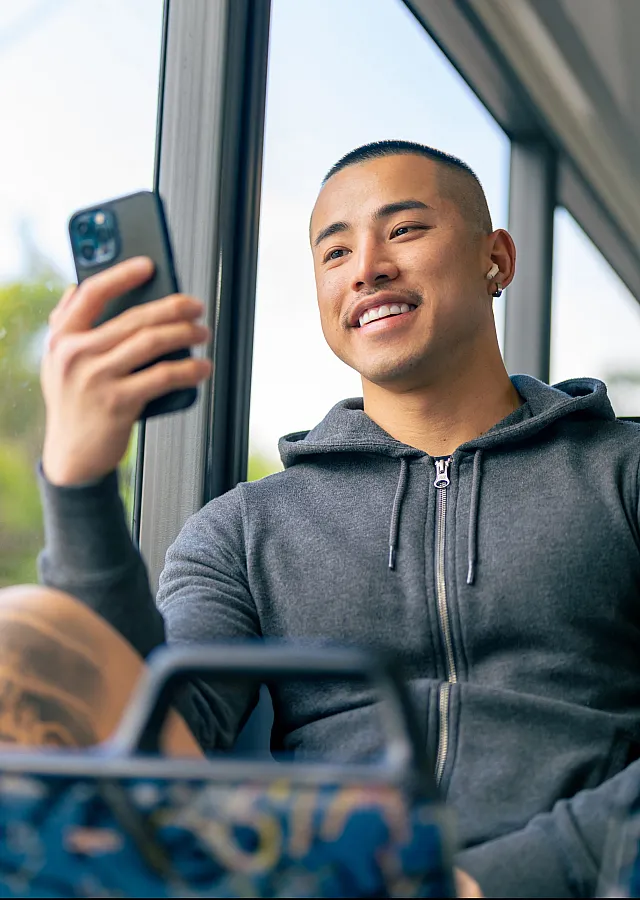 Smiling individual in a hoodie enjoying a relaxing journey on public transport with lush greenery outside.