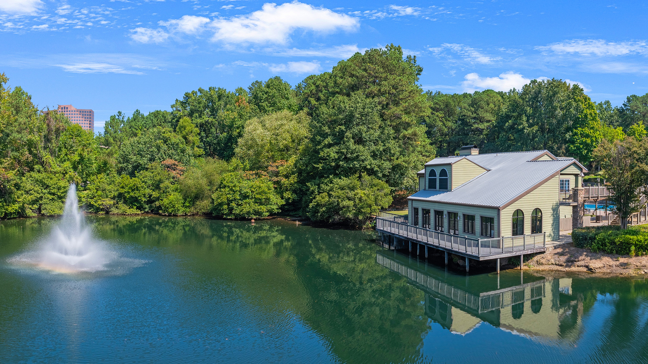 Charming lakeside house with spacious deck, nestled in lush greenery and serene water views, featuring a picturesque fountain in the foreground.