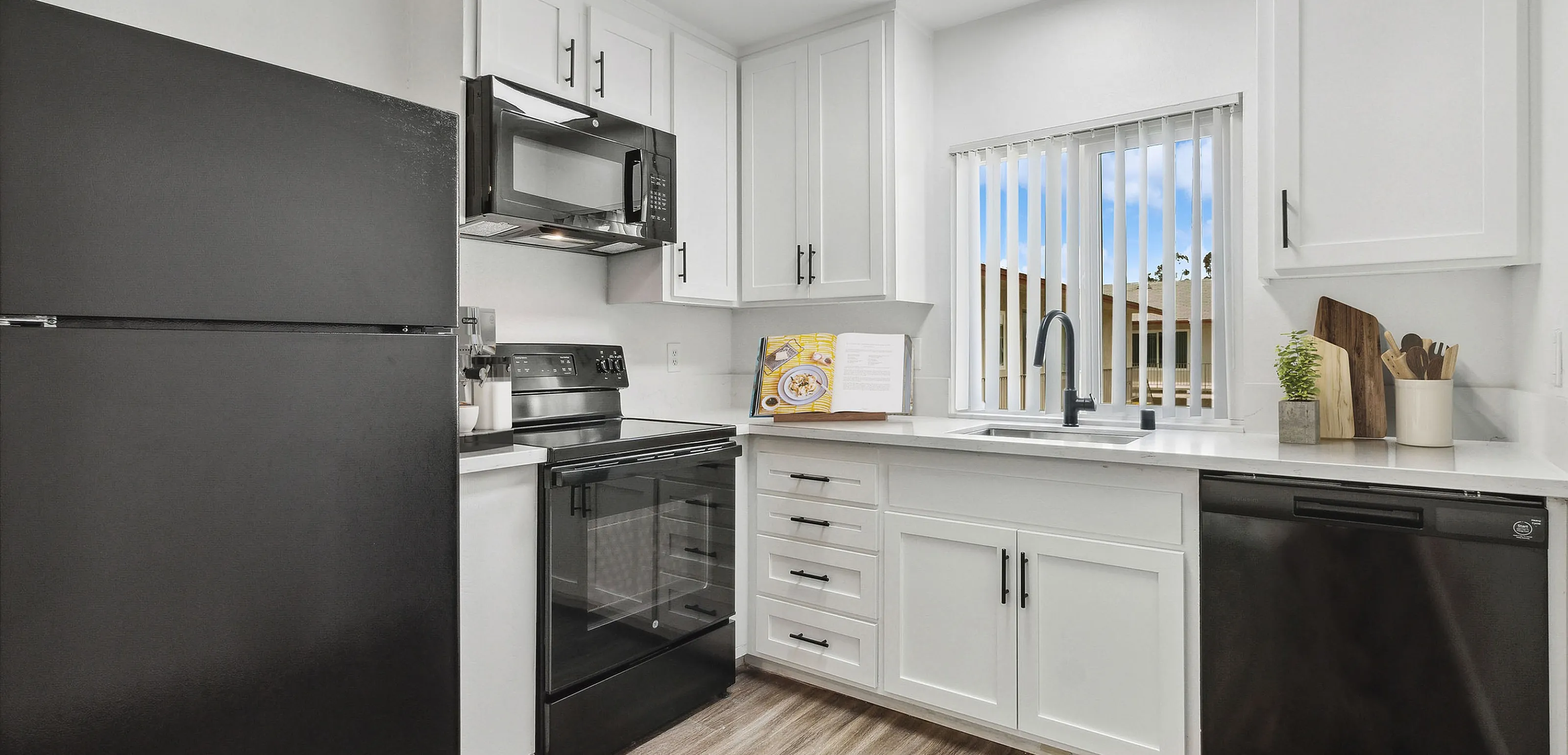 Modern kitchen with sleek black appliances, elegant white cabinetry, and a bright window view.