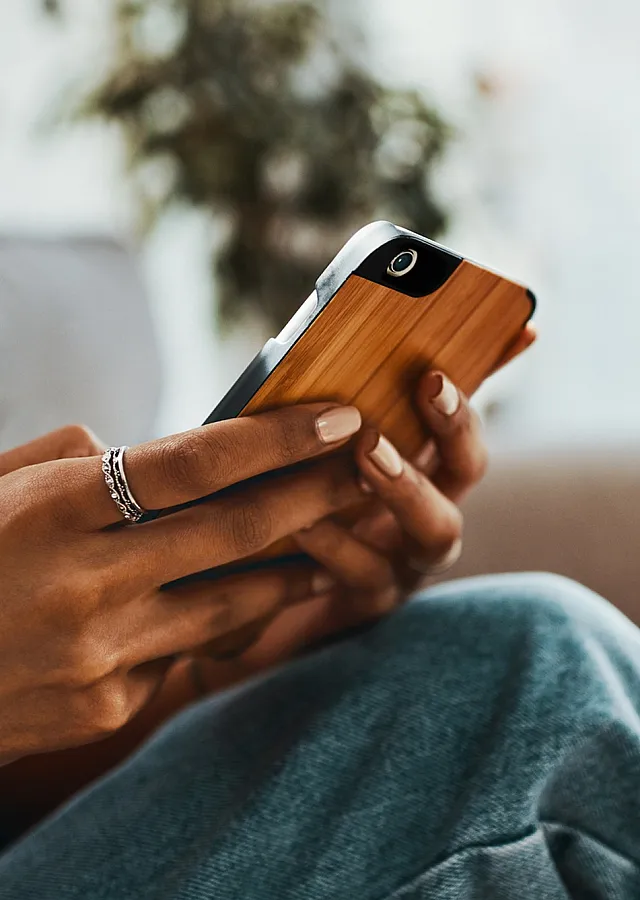 Close-up of a person using a smartphone with a stylish wooden case, seated on a cozy sofa.