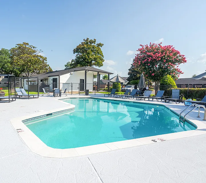 Inviting outdoor pool area with modern sun loungers, surrounded by lush greenery and vibrant flowers, perfect for relaxation in a tranquil setting.