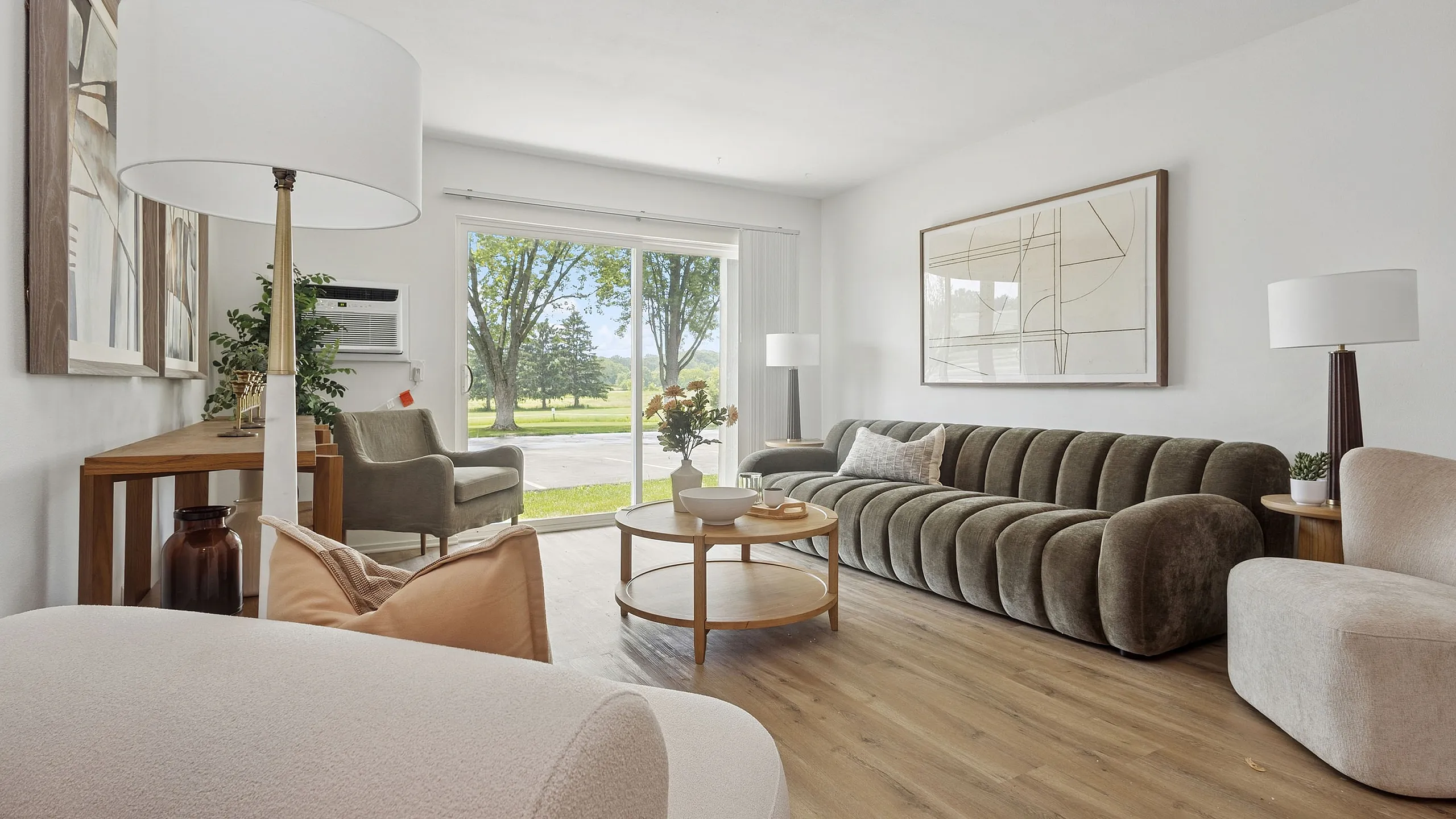 Bright and inviting living room with modern decor, featuring a plush green sofa, stylish round coffee table, and large floor-to-ceiling window showcasing a scenic outdoor view.