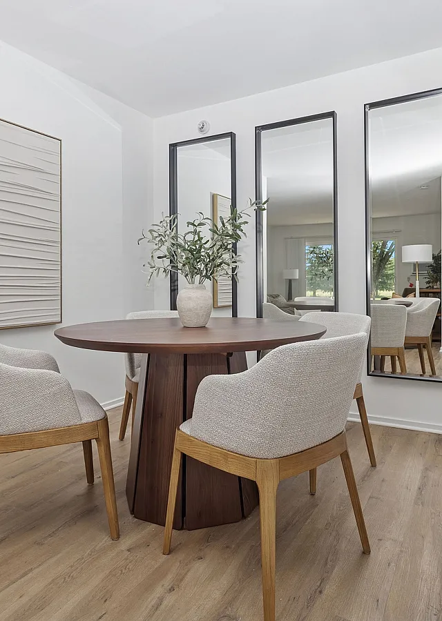 Elegant dining area featuring a modern round wooden table, plush upholstered chairs, and stylish mirrors, creating a chic and inviting atmosphere.