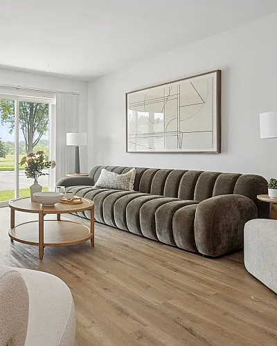 Bright and inviting living room with a modern velvet sofa, chic decor, and large windows overlooking a serene outdoor view.