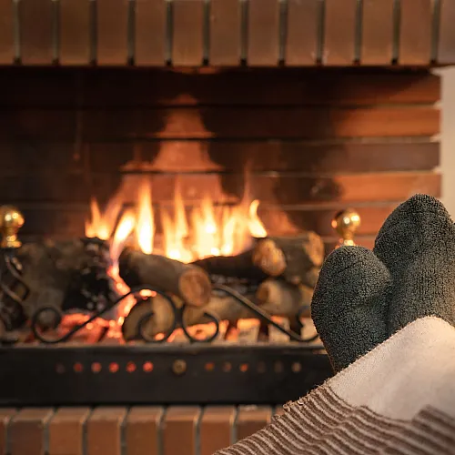 Cozy living room scene with a warm brick fireplace, roaring fire, and feet in cozy socks resting on a blanket, creating a perfect relaxing ambiance.