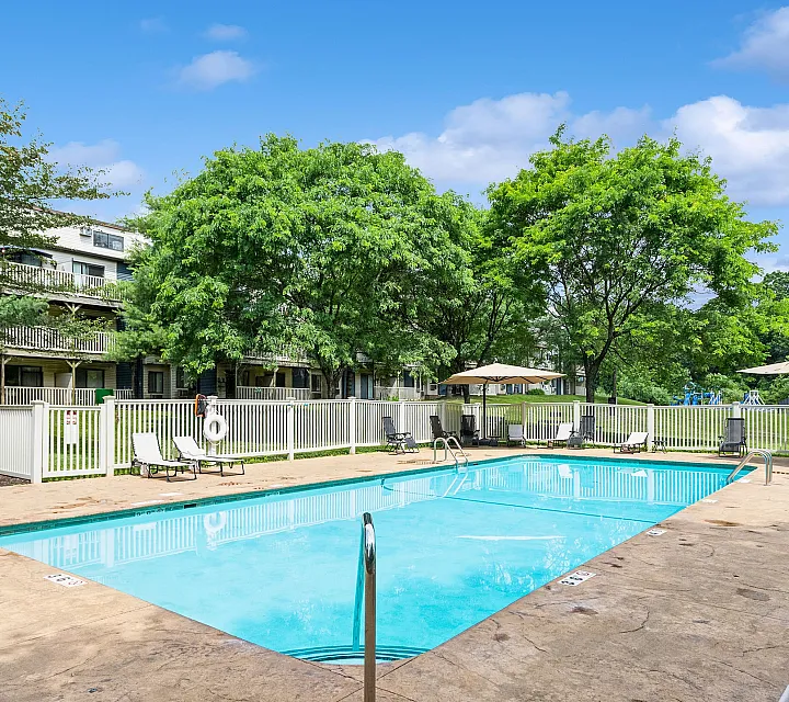 Inviting apartment complex with a refreshing outdoor pool surrounded by lush greenery and lounge chairs, perfect for relaxation and leisure.