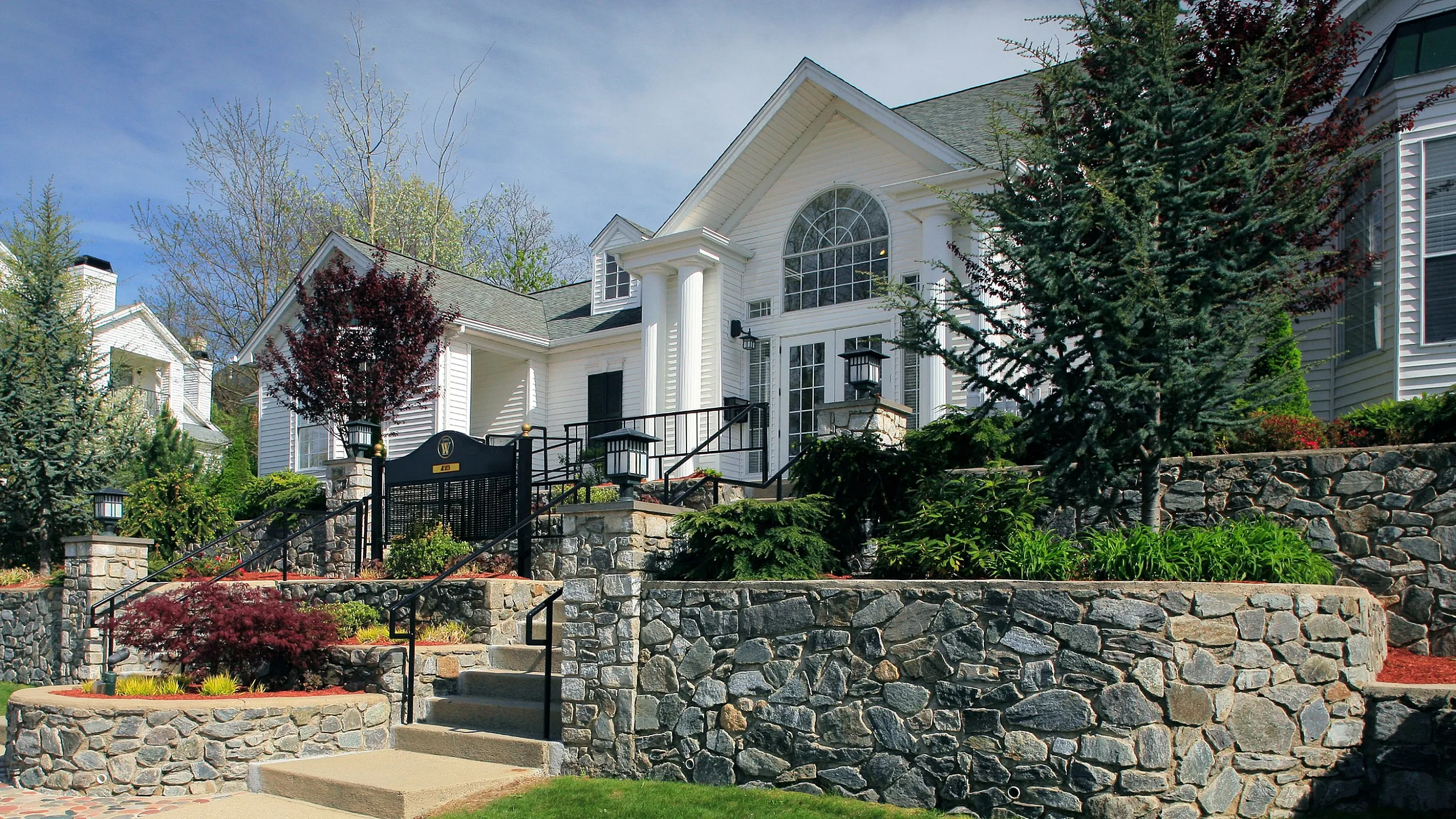 Charming colonial-style apartment building with elegant stonework and lush landscaping under a clear blue sky.
