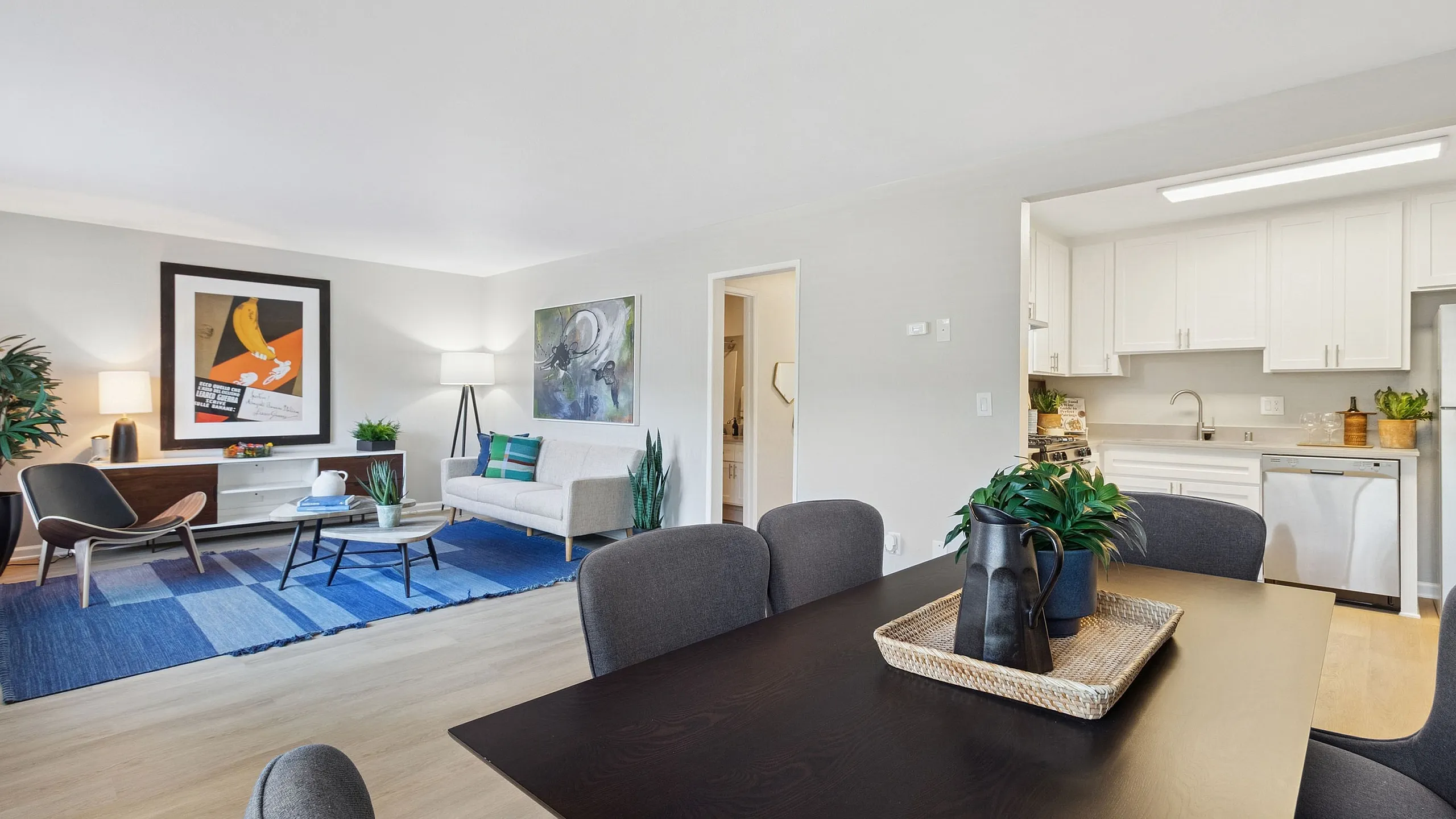 Modern open-plan living space with sleek dining area, cozy seating, and a bright kitchen, accented by stylish decor and vibrant artwork.
