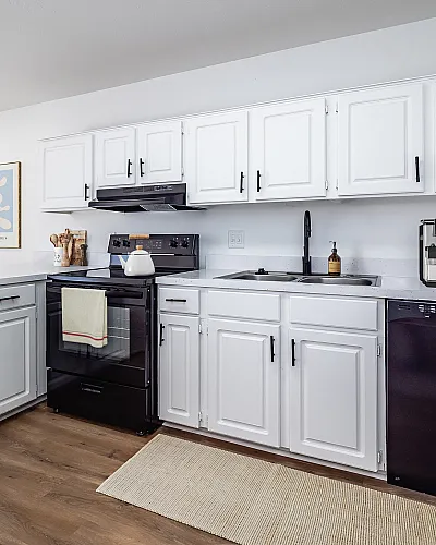 Charming modern kitchen with sleek black appliances, white cabinetry, and cozy wood flooring. Ideal for culinary enthusiasts.