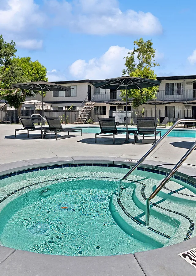 Inviting apartment complex pool area featuring a bubbling hot tub and cozy lounge chairs, perfect for relaxation and sunbathing.
