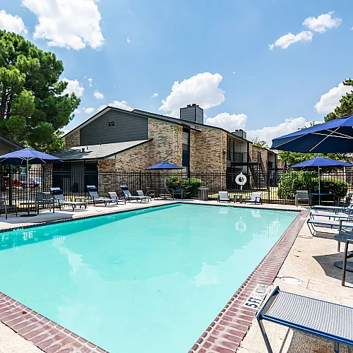 Inviting outdoor pool area with sun loungers and umbrellas set against a backdrop of charming brick apartments, perfect for relaxation and leisure.