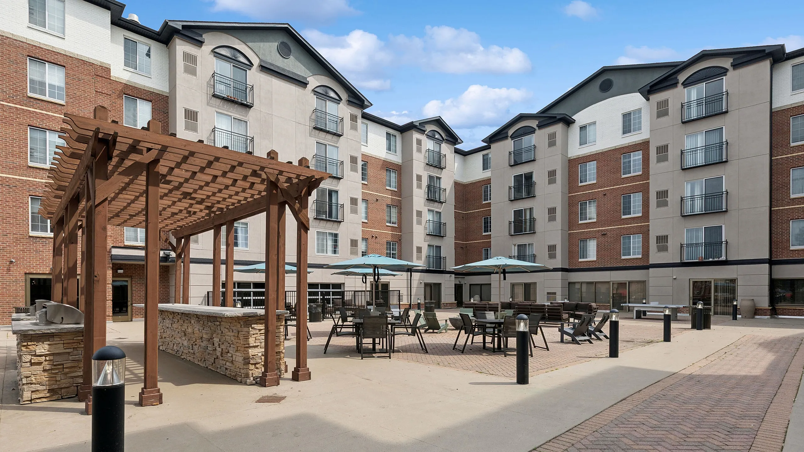Charming apartment courtyard featuring elegant pergola, outdoor seating, and modern brick architecture&mdash;perfect for social gatherings.