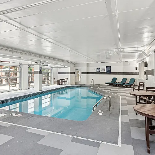 Luxurious indoor pool area with sleek modern design, featuring comfortable lounge chairs and natural lighting through large windows.