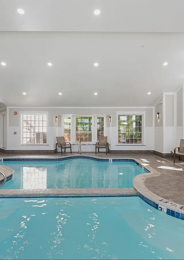 Elegant indoor pool area with modern design, featuring large windows, cozy seating, and a stylish fireplace for relaxation.