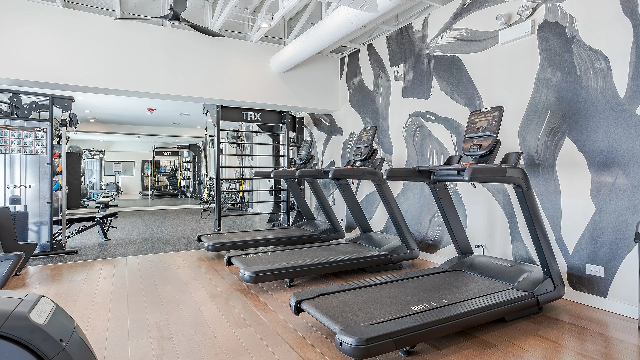 Modern fitness center featuring sleek treadmills, TRX equipment, and vibrant wall art on elegant wooden flooring.