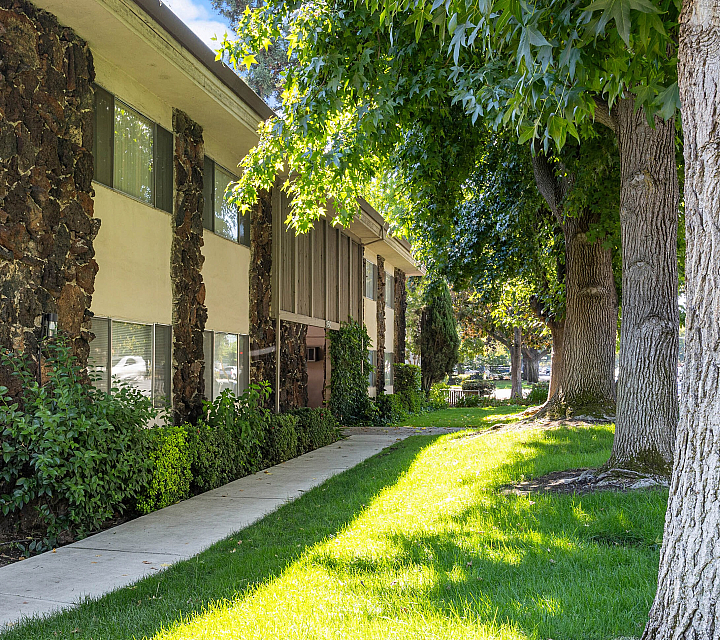 Charming apartment exterior with rustic stone accents, lush greenery, and inviting pathways under the shade of mature trees.