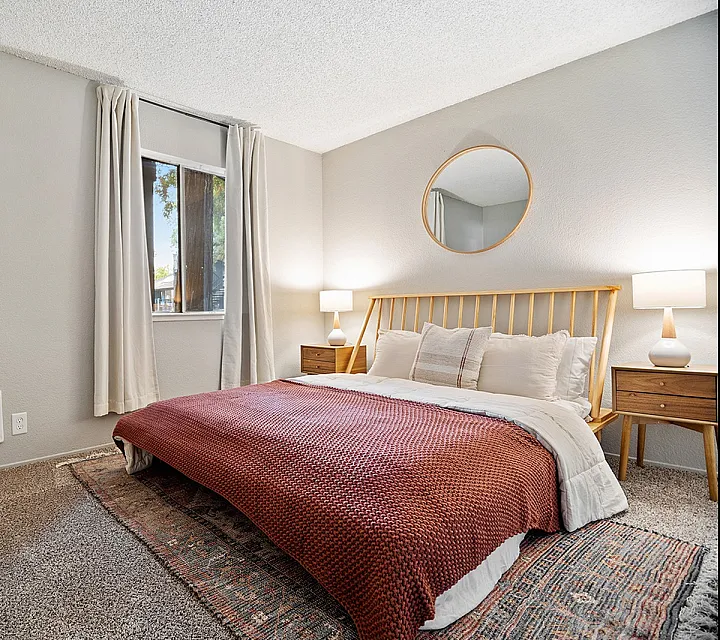 Cozy bedroom with modern design, featuring a plush, king-sized bed, soft lighting on elegant wooden nightstands, and a stylish circular mirror.