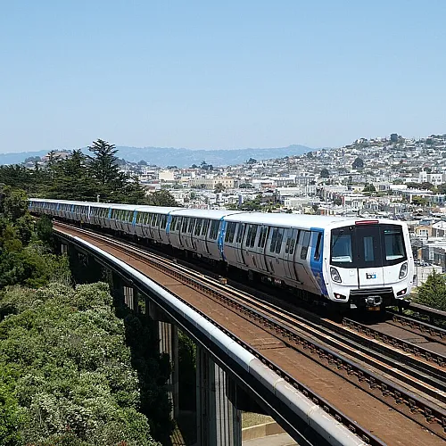 Dynamic urban view of a sleek metro train crossing an elevated track with scenic cityscape and lush greenery in the background.