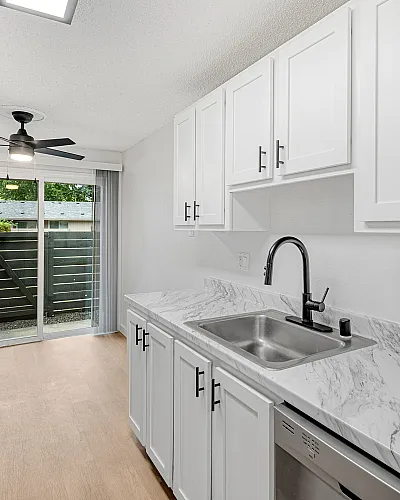 Modern kitchen with sleek white cabinetry, marble countertops, stainless steel appliances, and sliding doors leading to a private outdoor space.