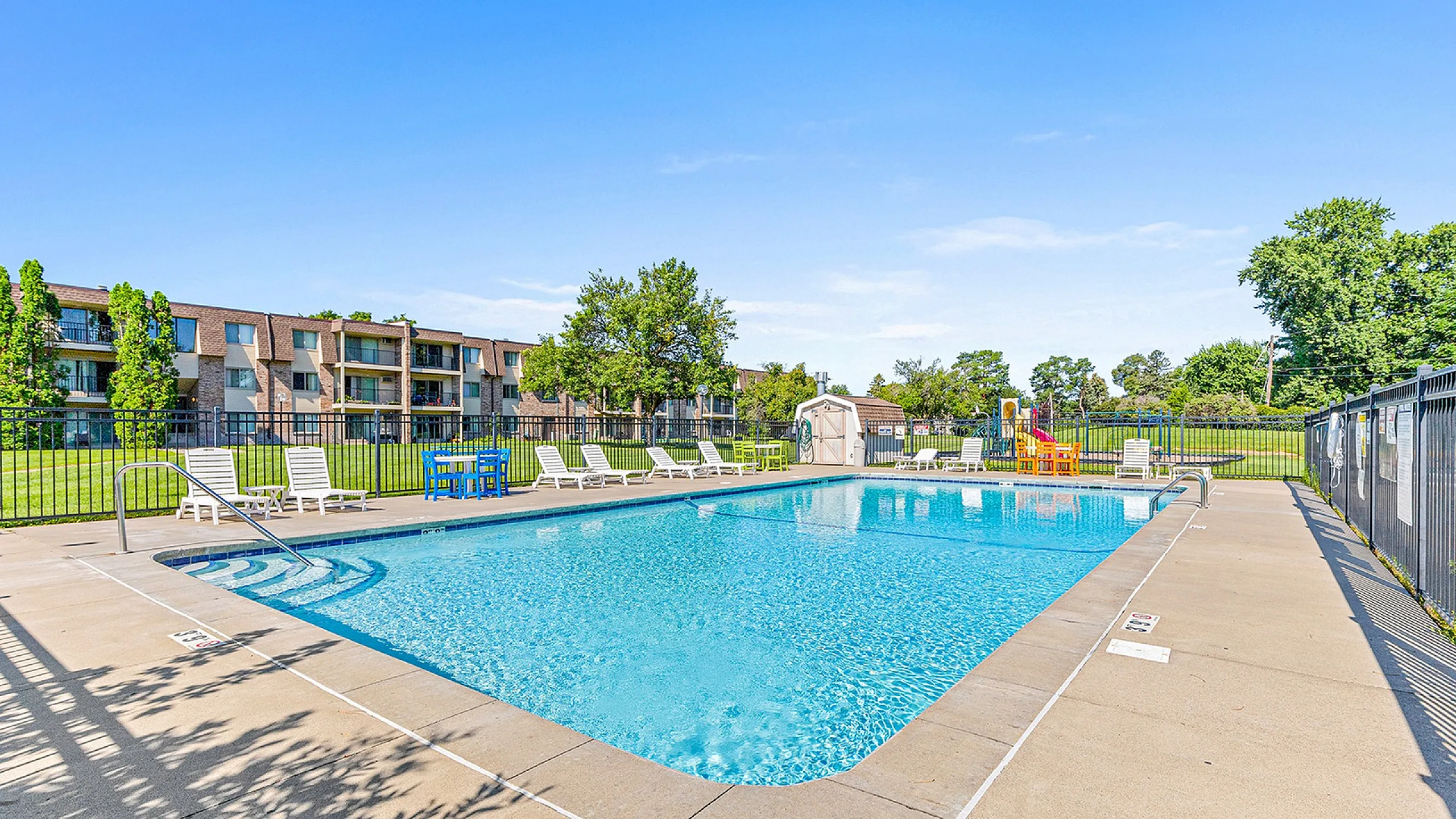 Renew at the Grove's inviting outdoor pool area with lounge chairs and a vibrant playground, set against a backdrop of well-maintained apartment buildings and lush greenery.