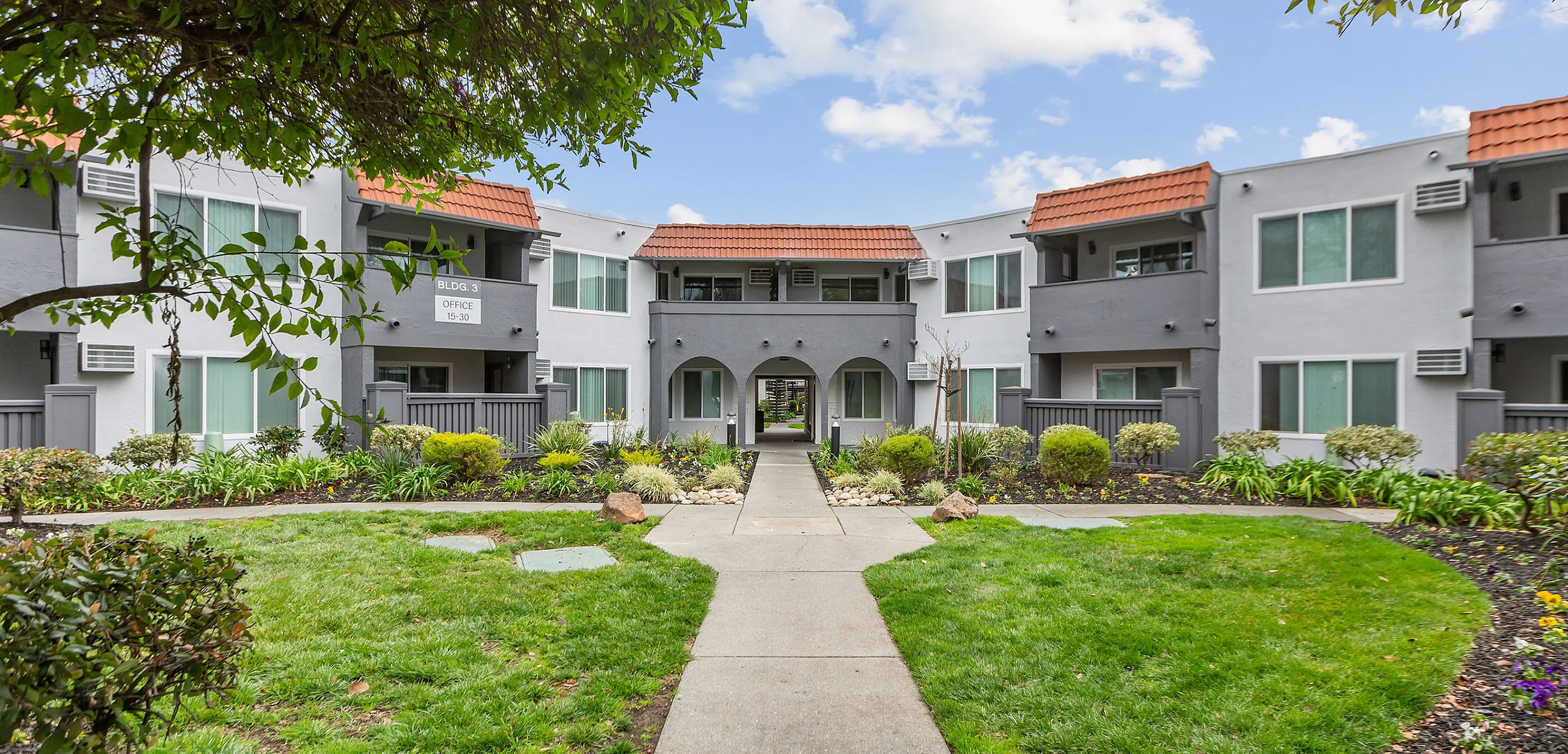 Charming two-story apartment building with modern design, lush landscaping, and a welcoming pathway leading to the entrance.