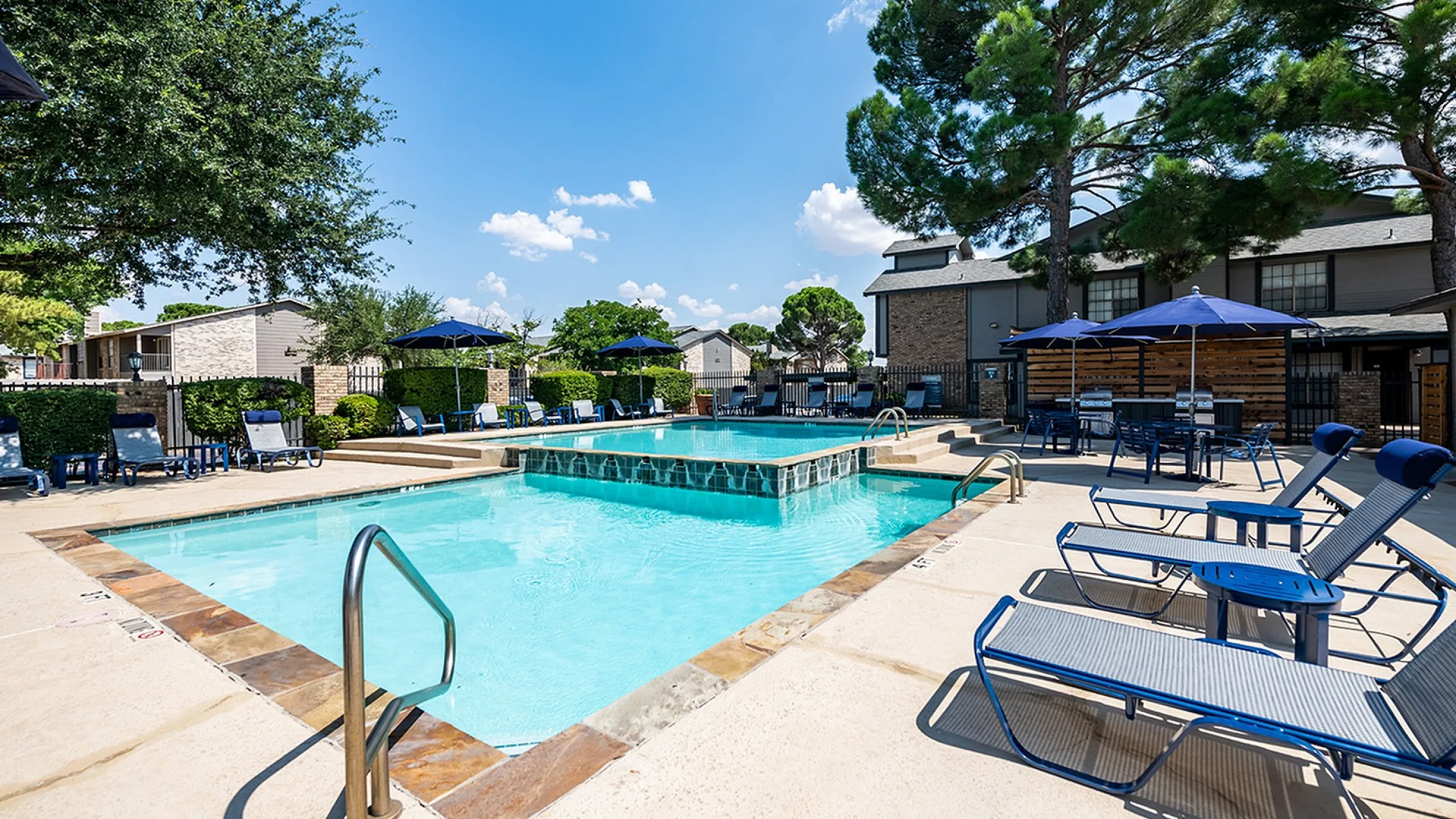 Inviting outdoor pool area at ReNew Holiday Hill with comfortable lounge chairs, pristine water, and shaded seating perfect for relaxation under a clear blue sky.