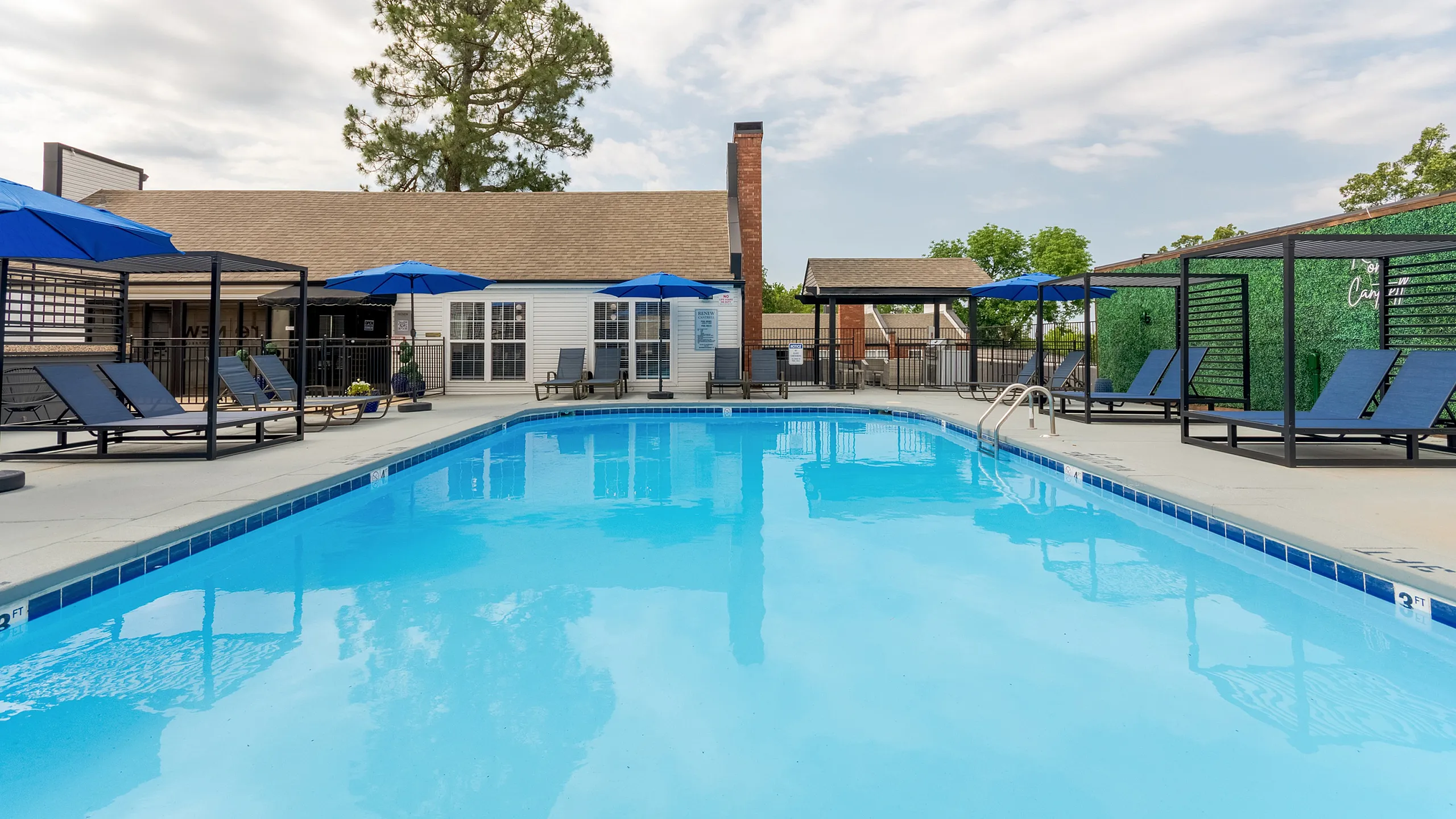 Inviting ReNew on Cantrell community pool area featuring blue sun loungers and vibrant umbrellas, surrounded by lush greenery and a charming clubhouse.