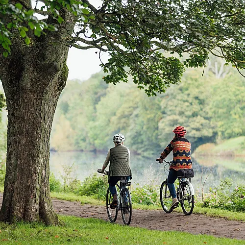 Scenic Two Rivers Park path with two cyclists enjoying a peaceful ride surrounded by lush greenery and tranquil water views.
