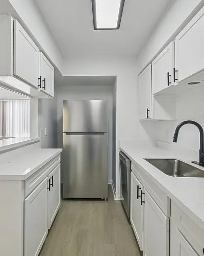 Bright and modern kitchen with sleek white cabinetry, stainless steel appliances, and an open view into the spacious living area.