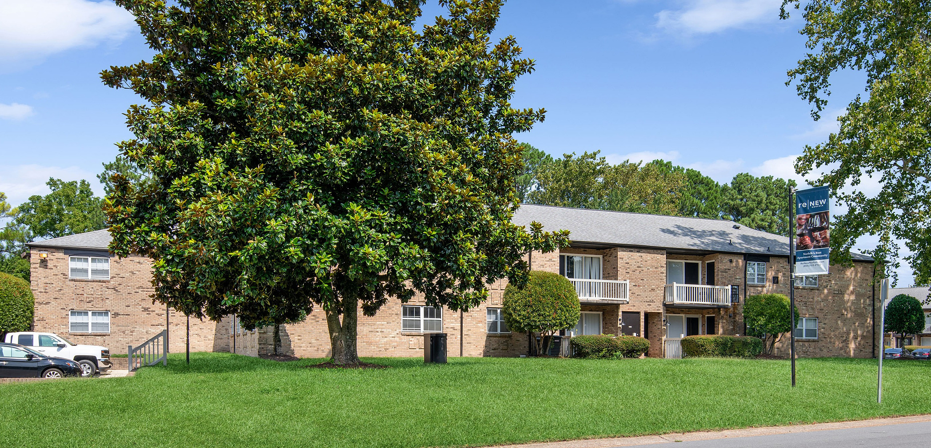 Charming brick apartment complex surrounded by lush greenery and mature trees, offering tranquil outdoor spaces and ample parking.
