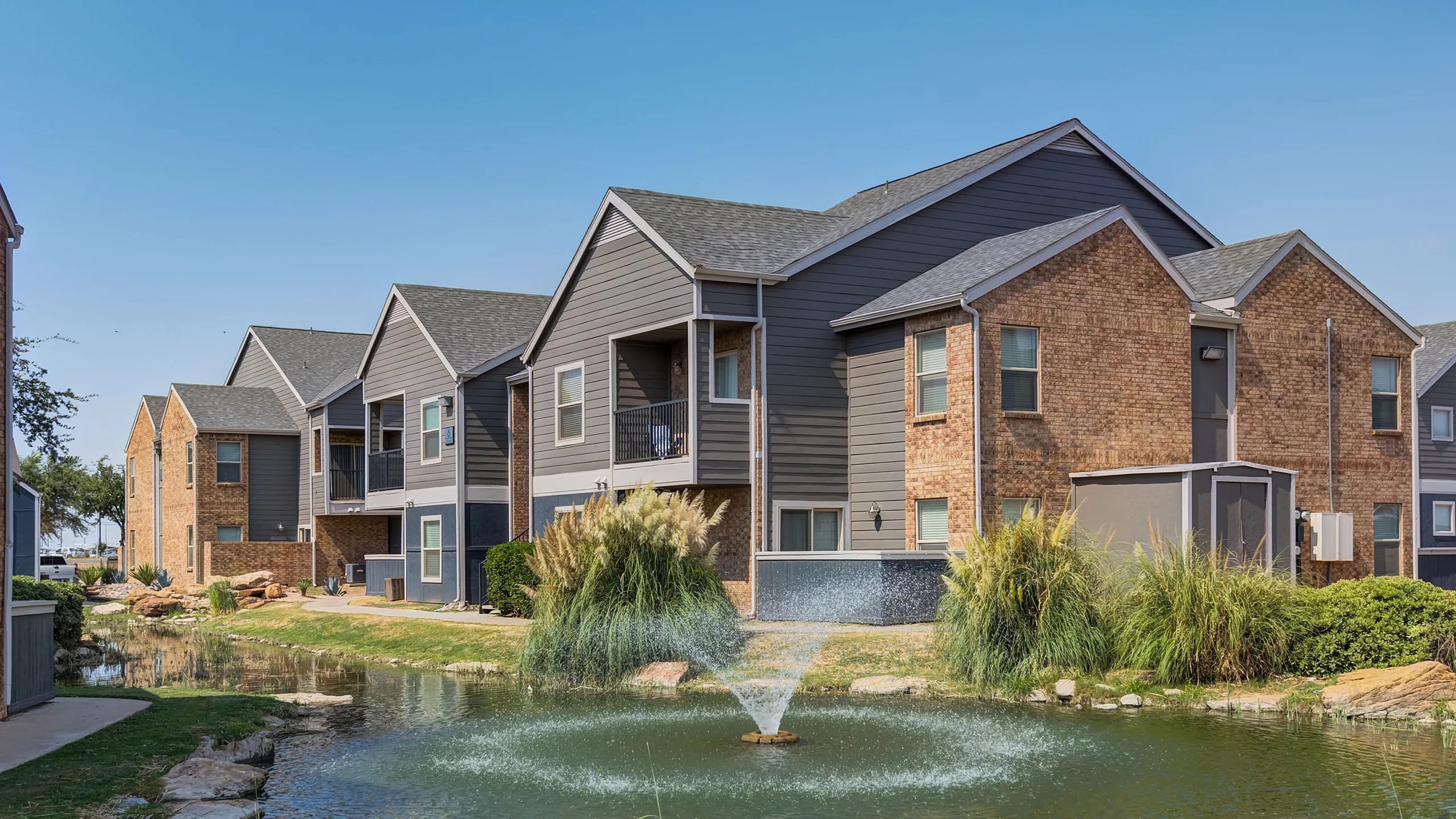 Charming ReNew Midland apartment complex surrounded by lush landscaping and a serene pond with a water fountain.
