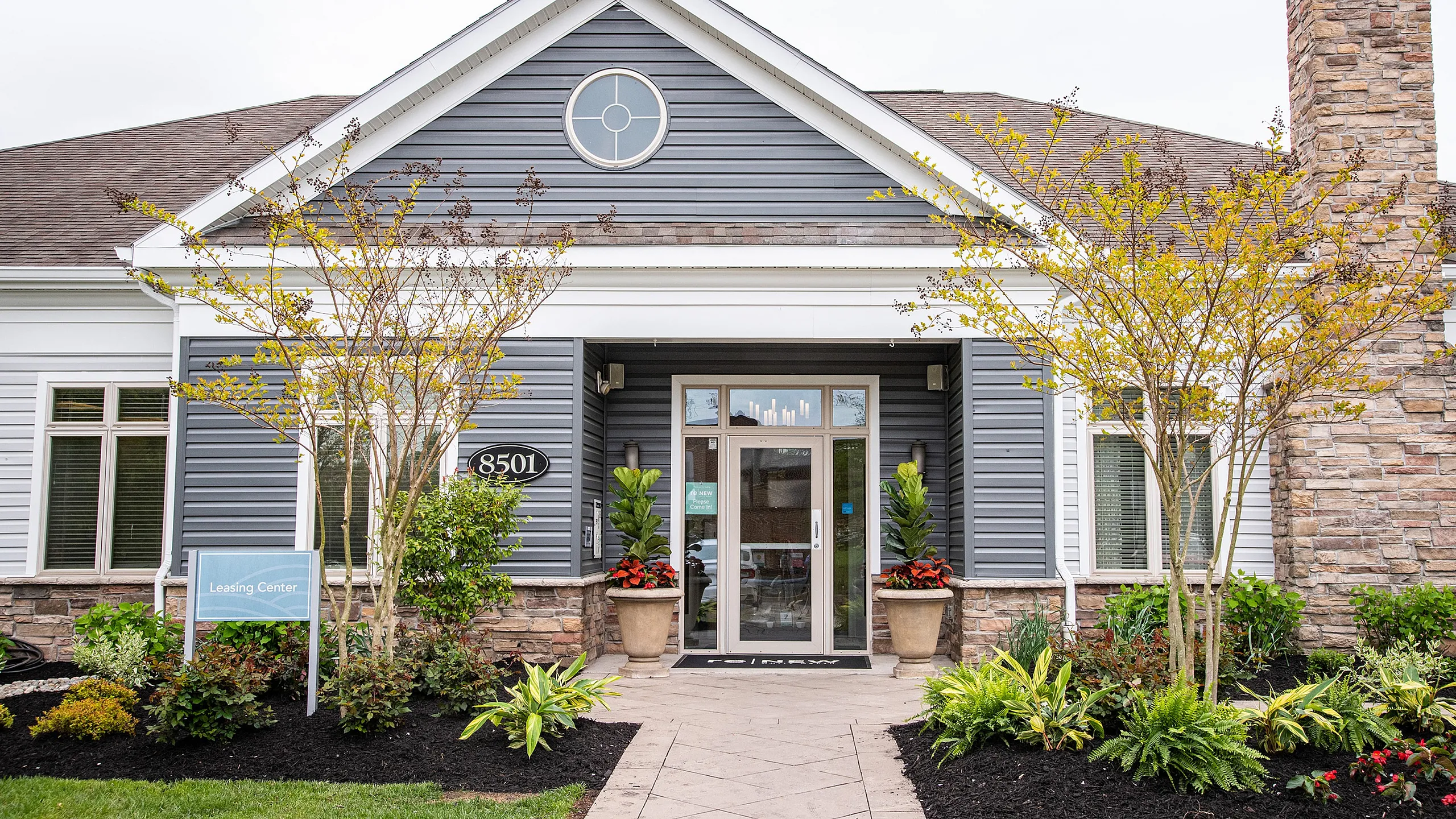 Charming leasing center at ReNew White Marsh entrance with modern architecture, elegant stone detailing, and vibrant landscaping, inviting you into a cozy home community.