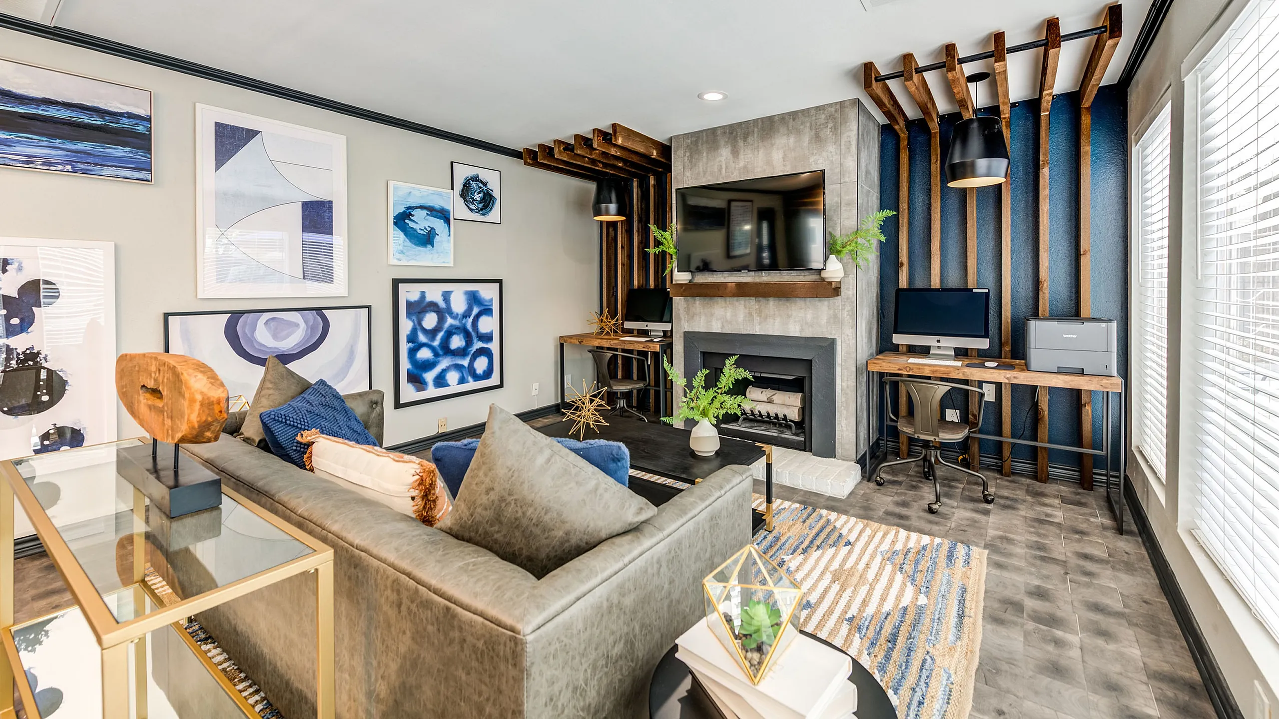 Modern living room at ReNew Heights with stylish decor, featuring a sleek fireplace, built-in desk with a computer, and vibrant wall art. Large window allows natural light to fill this inviting space.