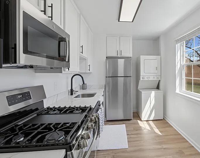 Modern kitchen at ReNew Howard Crossing with sleek stainless steel appliances, quartz countertops, and ample natural light from a large window.