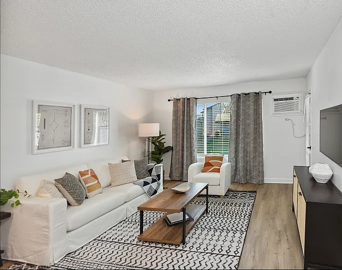 Elegant living room at ReNew Berryessa  with modern decor, featuring a cozy white sofa accented with colorful cushions, stylish coffee table, chic rug, and large window providing ample natural light.