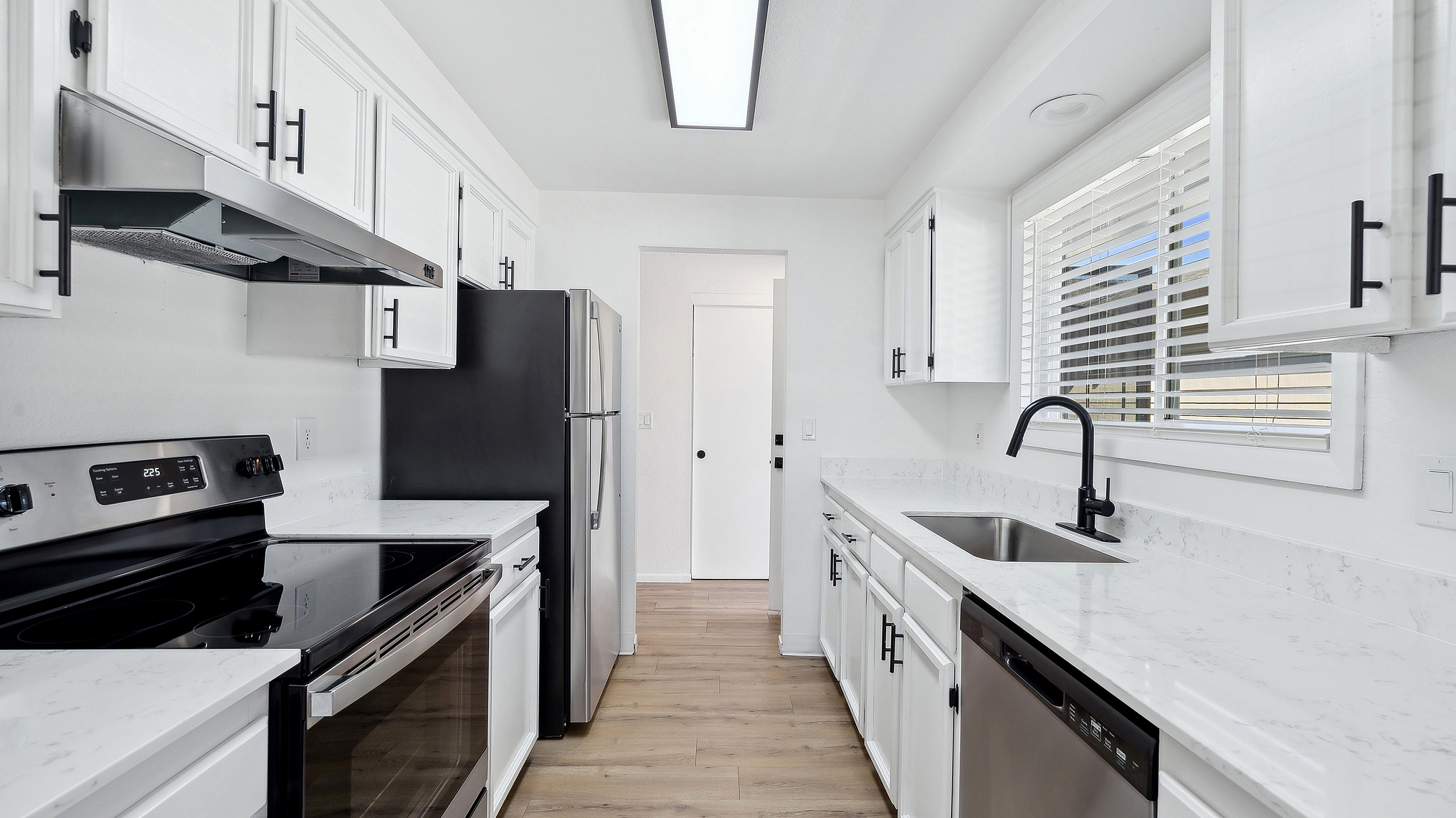 Sleek modern kitchen at ReNew Rock Creek featuring elegant white cabinetry, stainless steel appliances, and a large window for natural light.