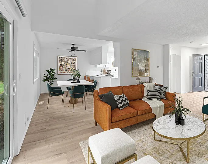 Bright and modern open-concept living space at ReNew Rock Creek featuring a cozy orange sofa, elegant dining area, and a sleek kitchen, highlighted by a large window with a view of lush greenery.