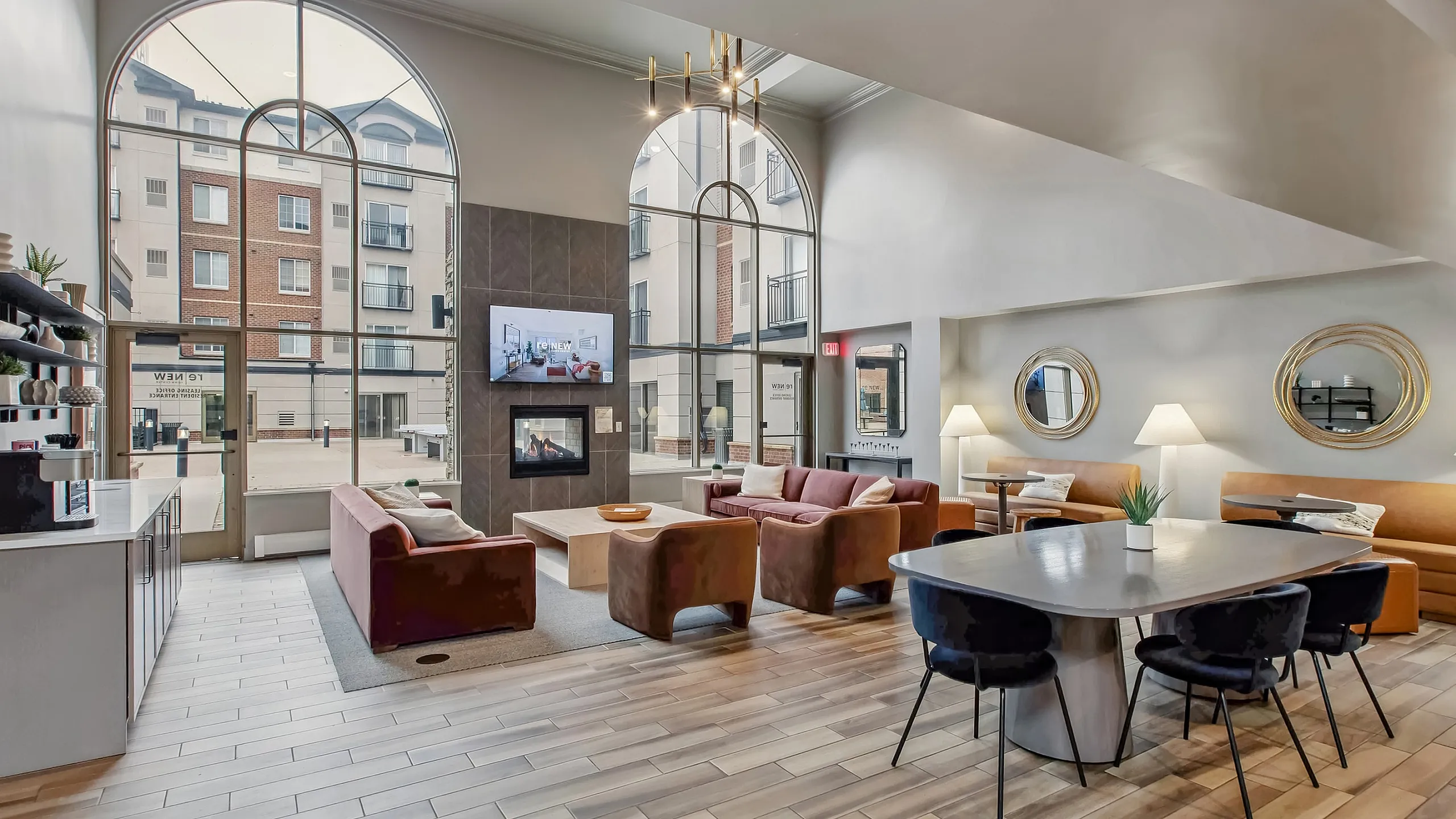 Elegant apartment lounge with modern decor, featuring stylish brown sofas, a cozy fireplace, and large arched windows providing abundant natural light.