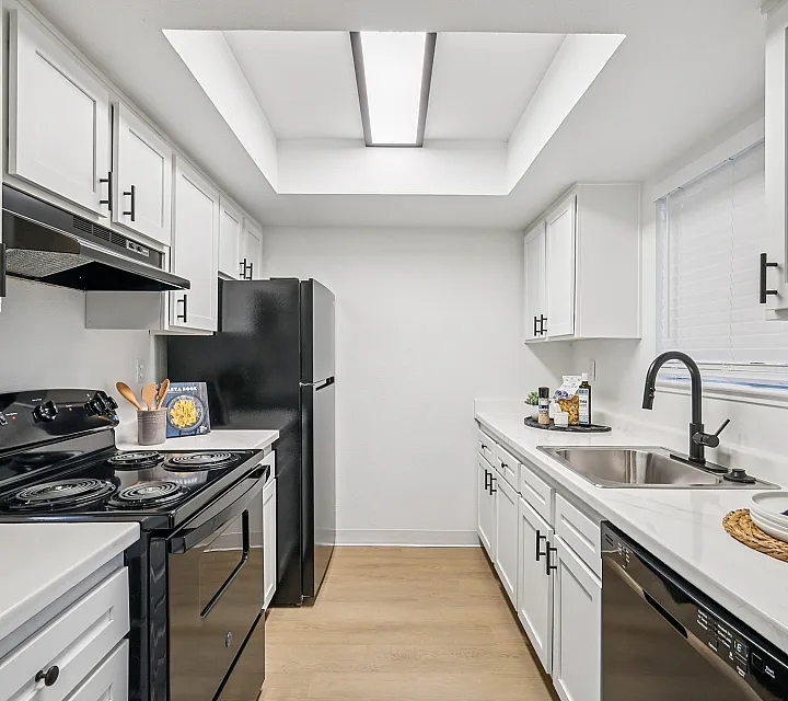 Elegant modern kitchen with sleek white cabinetry, black appliances, and sunlit workspace.