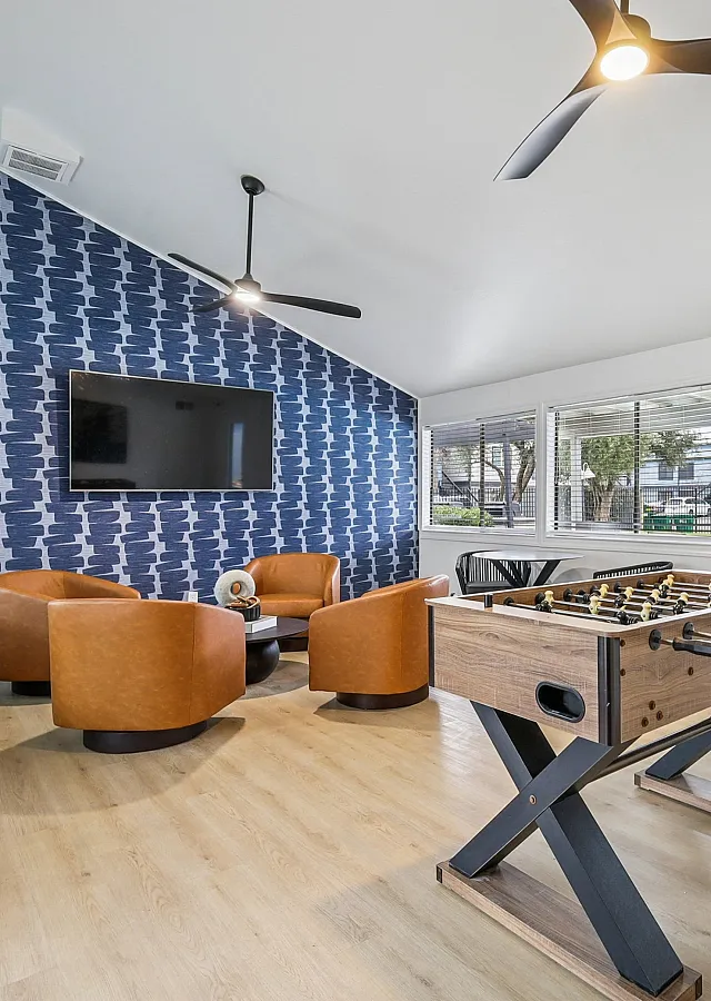Chic and modern recreation room featuring sleek ceiling fans, plush leather seating, and a foosball table, overlooking a sunlit pool area.