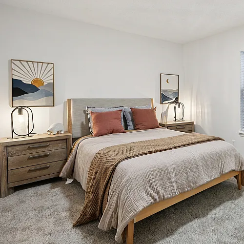 Inviting bedroom showcasing a cozy double bed with soft pillows, warm lighting, and serene artwork, complemented by plush carpeting and natural light from a large window.