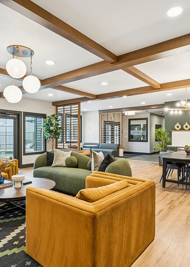 Spacious open-concept living room with stylish modern furniture, large windows, wooden ceiling beams, and a cozy dining area with chic lighting.