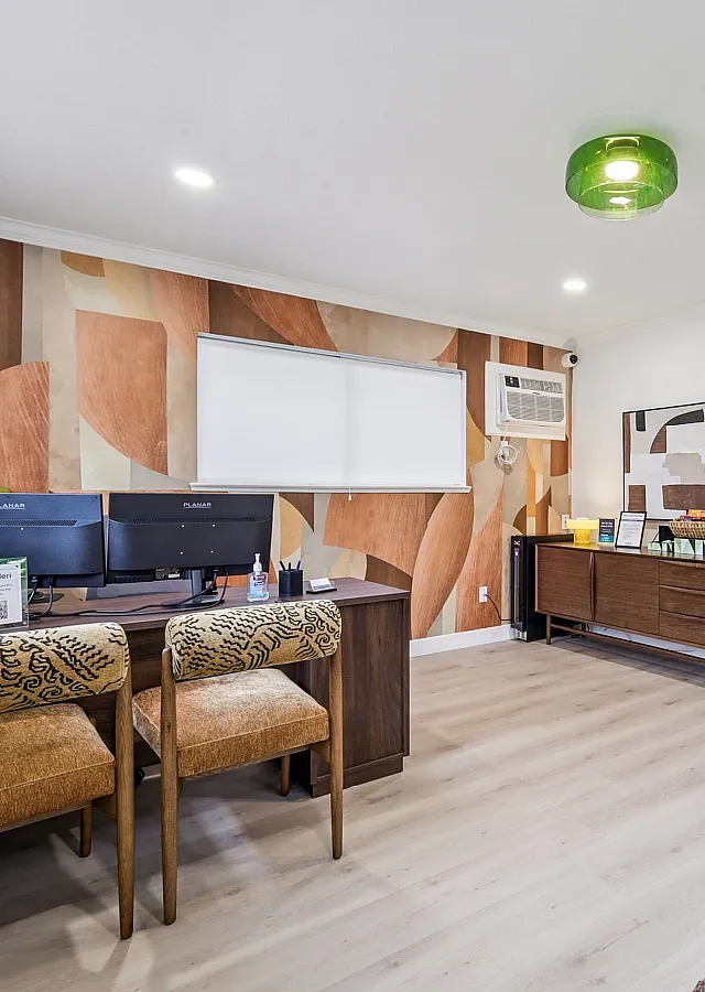 Chic home office with vibrant geometric wallpaper, modern wood furnishings, and twin computer monitors on an elegant desk.