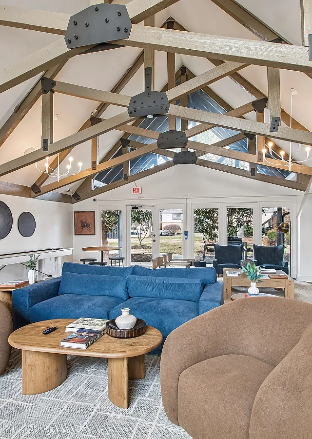 Charming living room with vaulted ceilings, exposed beams, cozy seating, and abundant natural light from large windows.